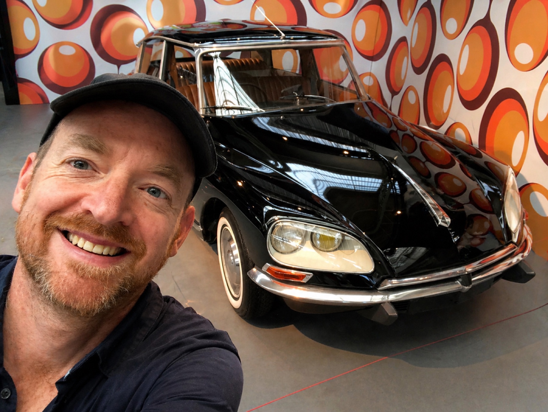 Tom Kenis smiling beside a black Citroën DS in a museum
